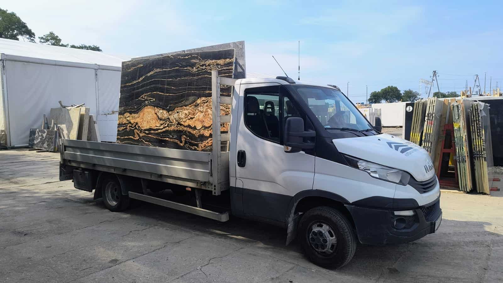 Auto nowe Złom biały samochód dostawczy z ciemną płytą granitową na tylnym bagażniku, przewóz naturalnego kamienia, szeroki wybór kamieni ozdobnych i konstrukcyjnych w ofercie firmy Global Stone.